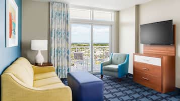 A hotel room with a balcony, a sofa, a chair, a TV, and a dresser.