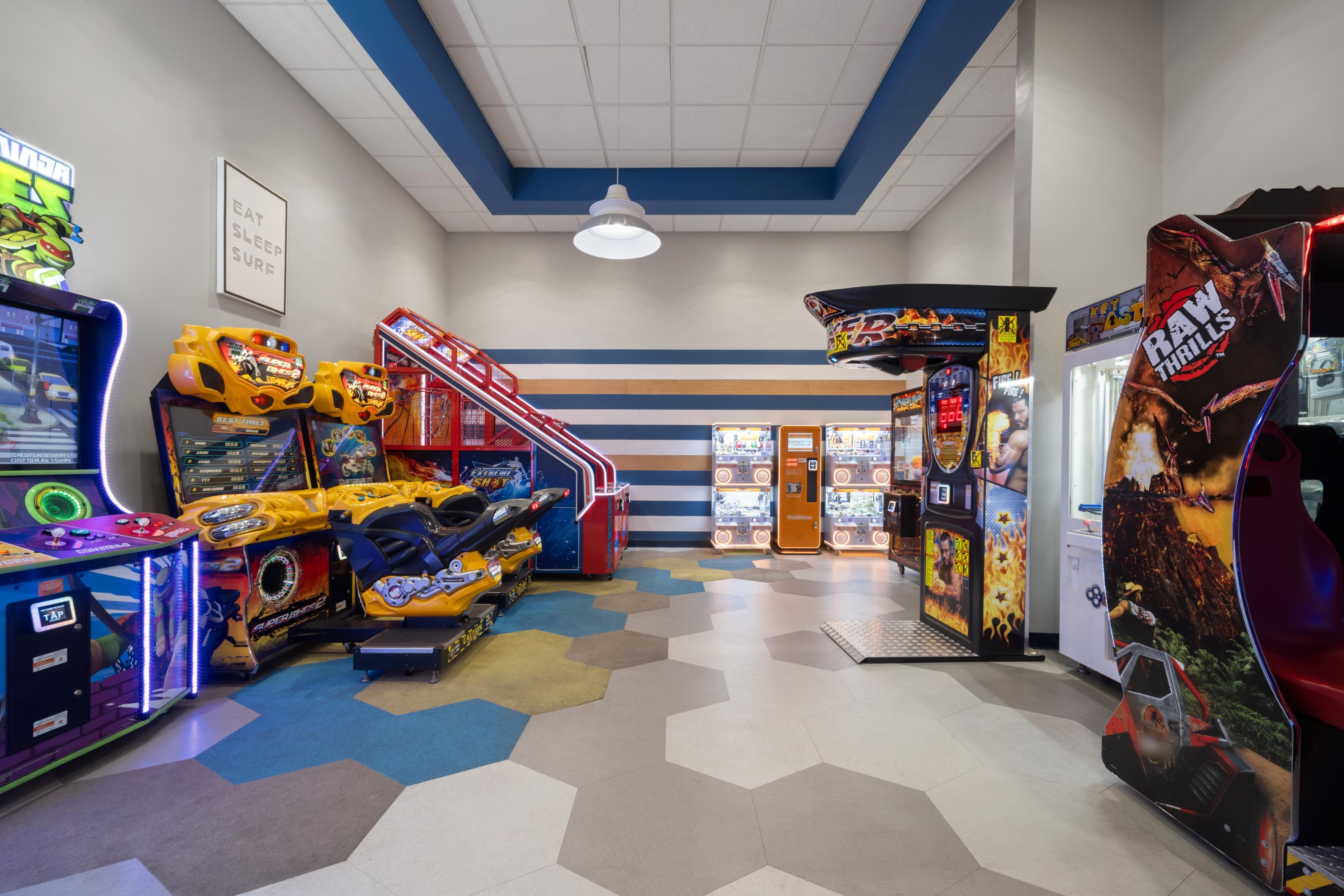 An arcade with various gaming machines, including racing and shooting games, and a vending machine.