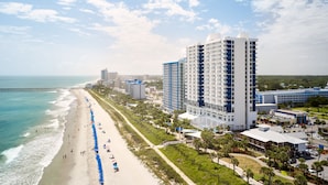 A coastal hotel with a beach view, multiple floors, and a parking area.