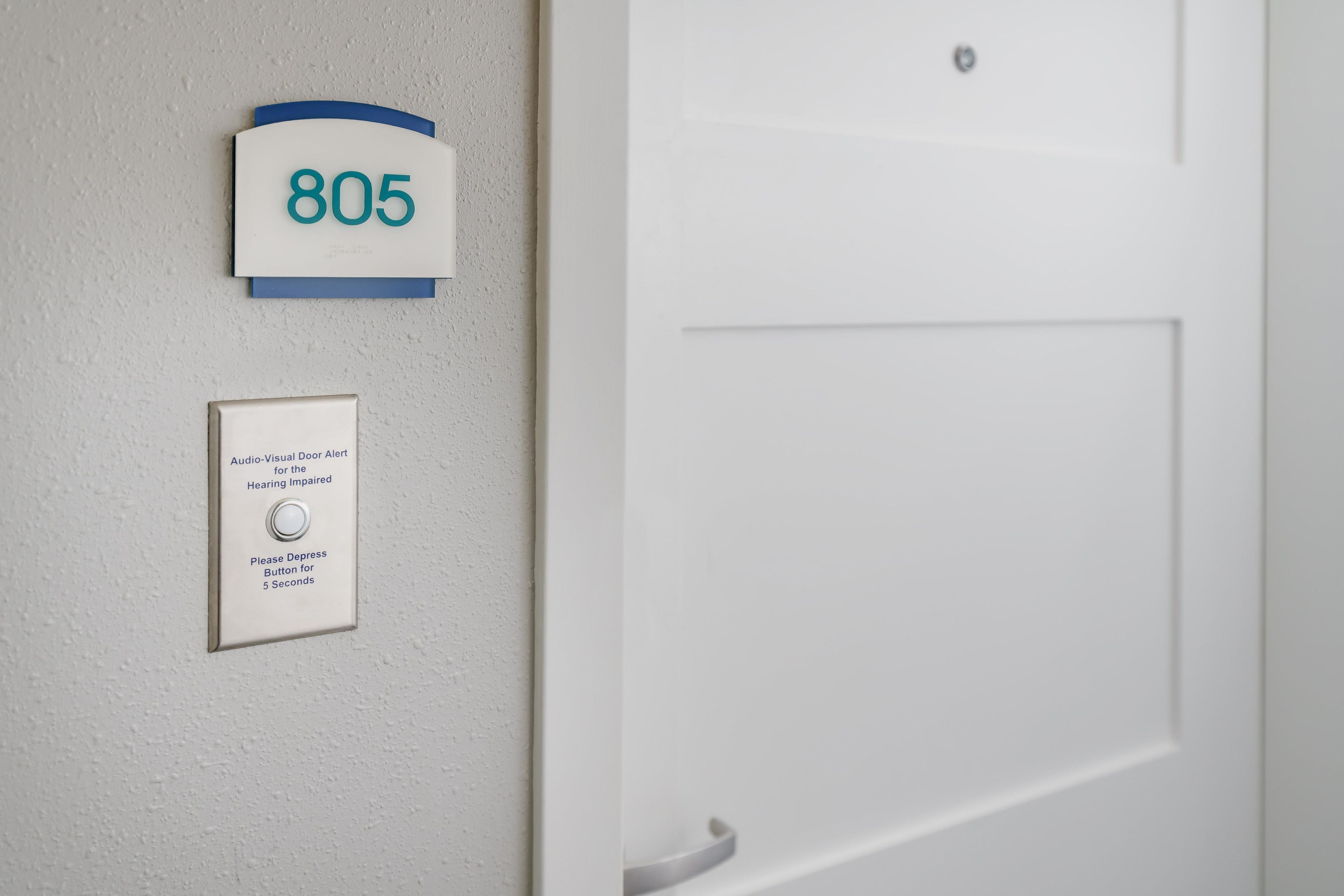 Uma porta com uma placa de identificação com o número '805' e uma placa abaixo indicando um alarme audiovisual para deficientes auditivos.