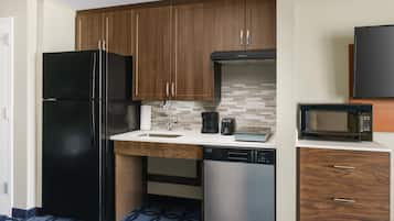 Cozinha compacta com geladeira preta, lava-louças de aço inoxidável e micro-ondas na bancada.