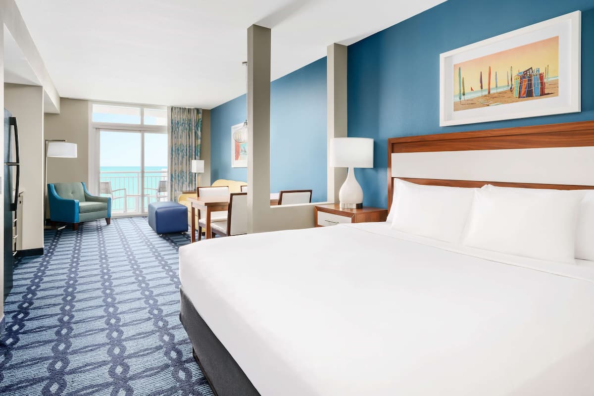 Una camera d'albergo con un letto grande, una scrivania, una sedia e vista sull'oceano.