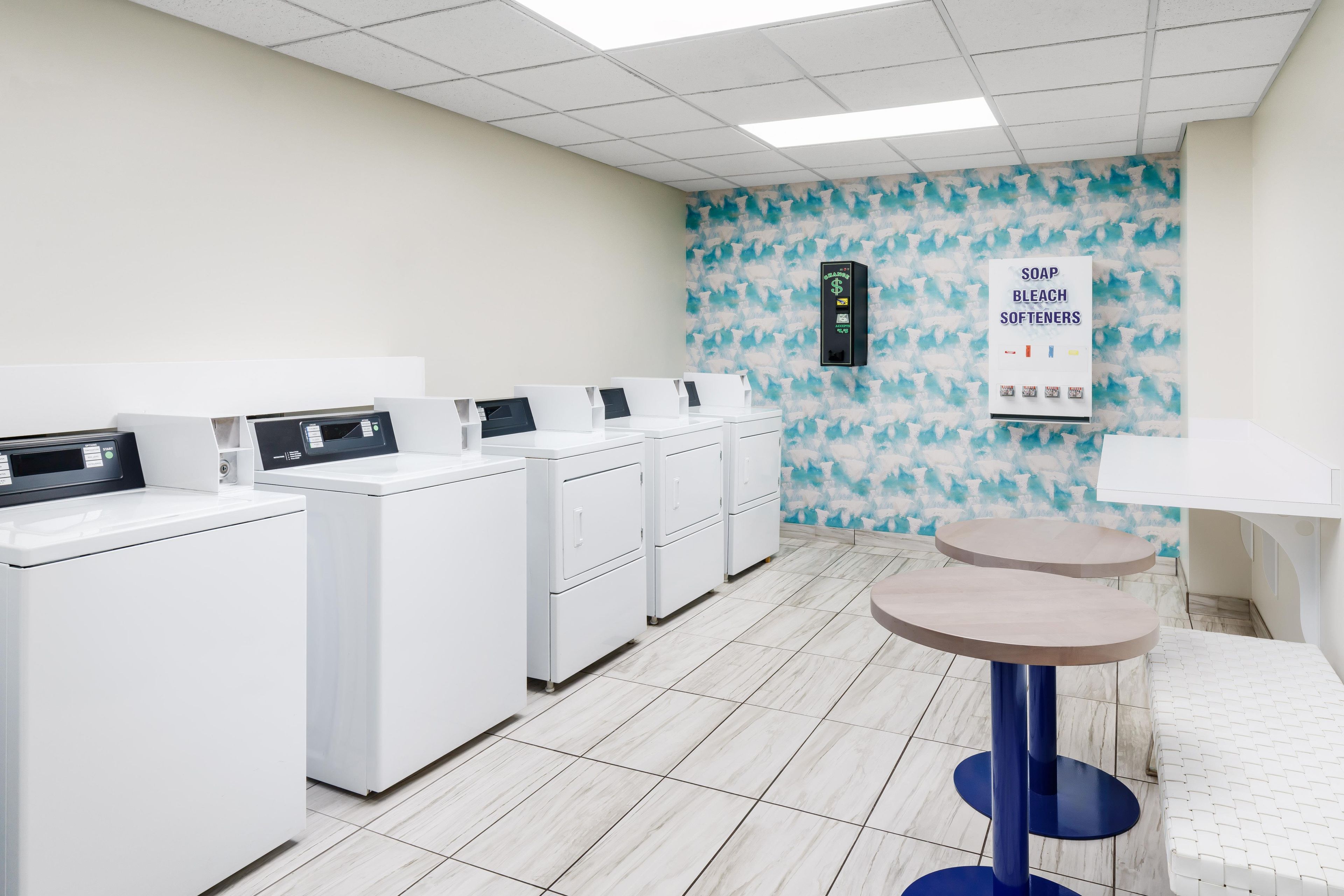 A laundry facility with multiple washing machines, a payment kiosk, and a wall-mounted soap and bleach dispenser.