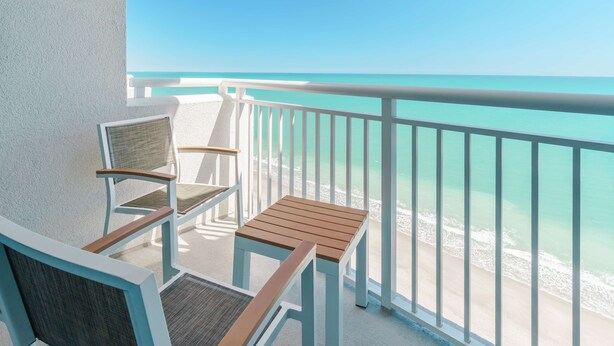 A balcony with a view of the ocean, featuring two wooden chairs and a small table.