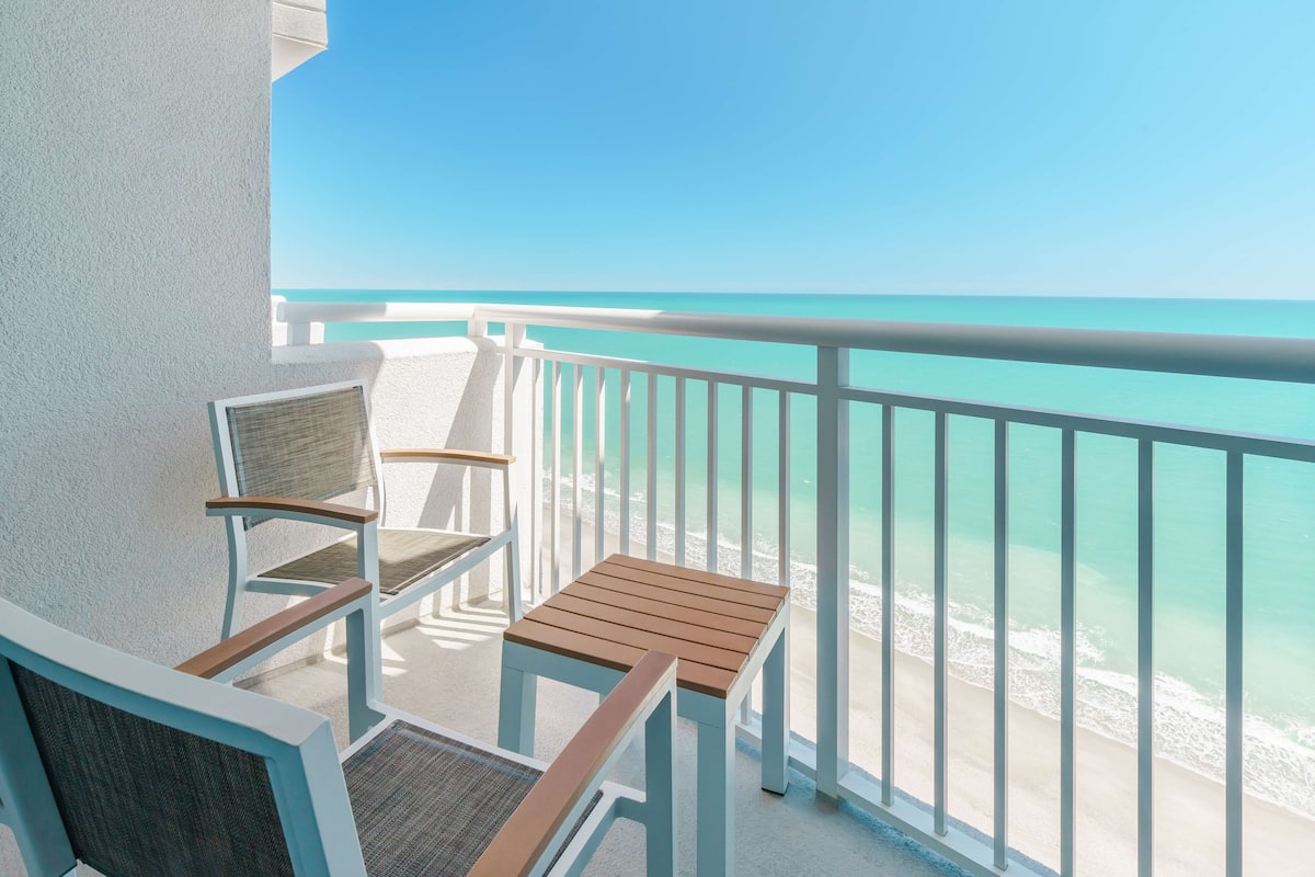 Un balcone con vista sull'oceano, dotato di due sedie di legno e un tavolino.
