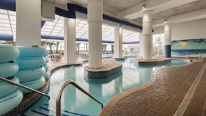 An indoor swimming pool with clear blue water, white columns, and a tiled deck area.