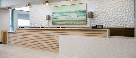A hotel reception desk with a textured wall, a large framed picture of a beach scene, and a sign indicating Hilton Honors.