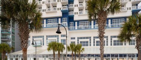 A modern hotel with multiple balconies, palm trees, and a covered outdoor area.