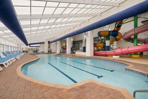 Una piscina interior con varias pistas de natación, un tobogán y sillas de descanso.