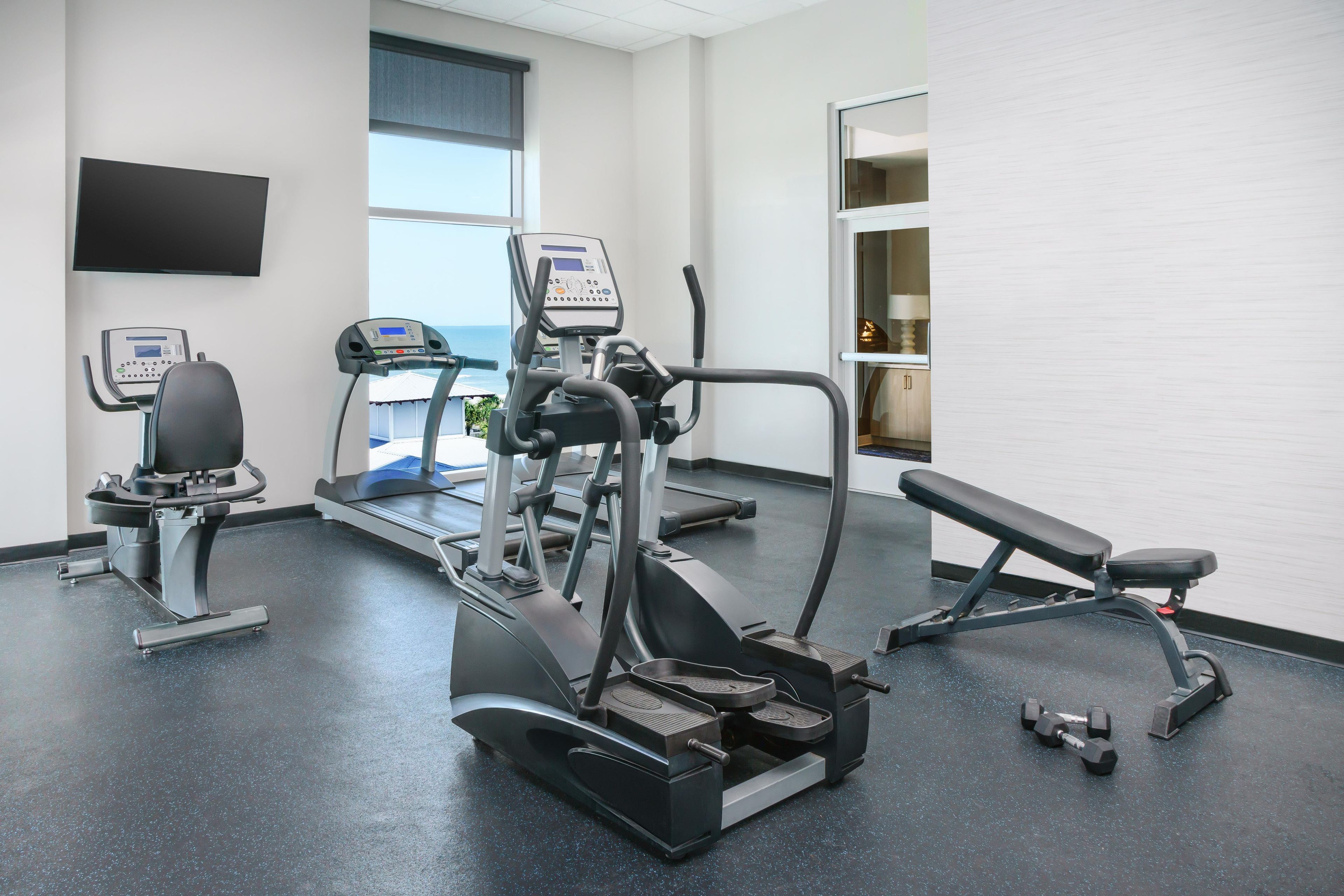 A gym with cardio machines, a bench, and dumbbells.