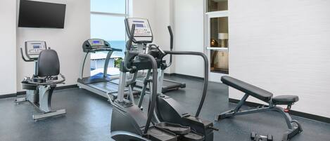 Une salle de sport équipée de machines de cardio, d’un banc et d’haltères.