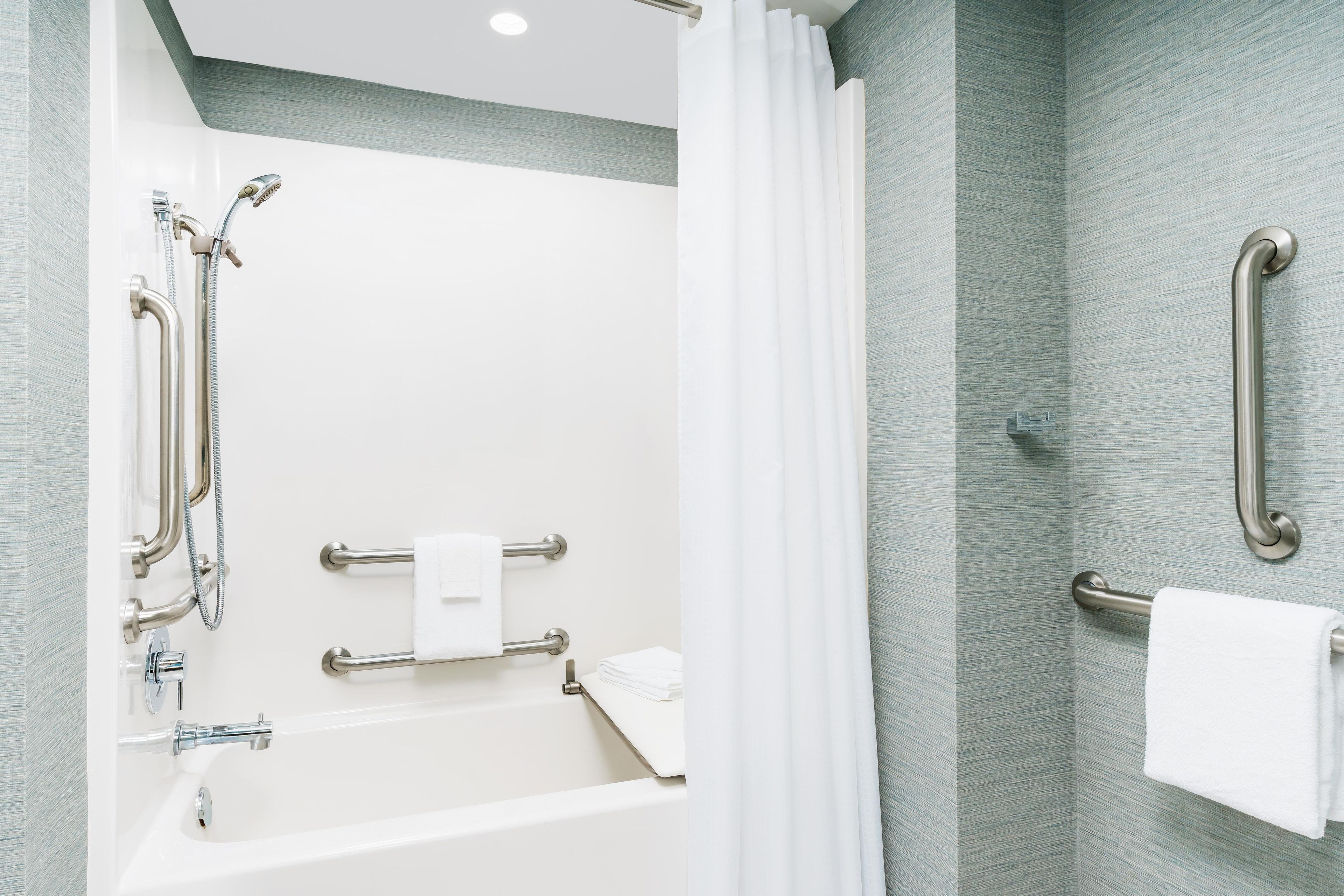 Ein modernes Badezimmer mit Badewanne, Dusche und Haltegriffen.