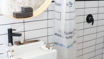 Une salle de bain avec un lavabo blanc, un robinet noir et un miroir au-dessus. Il y a un rideau de douche avec du texte imprimé dessus, et le sol est recouvert d’un motif à carreaux noirs et blancs.