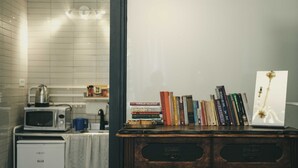A kitchenette with a microwave, kettle, and coffee maker, and a wooden cabinet with books and a decorative item. - Tzefania Hotel (Jerusalem)