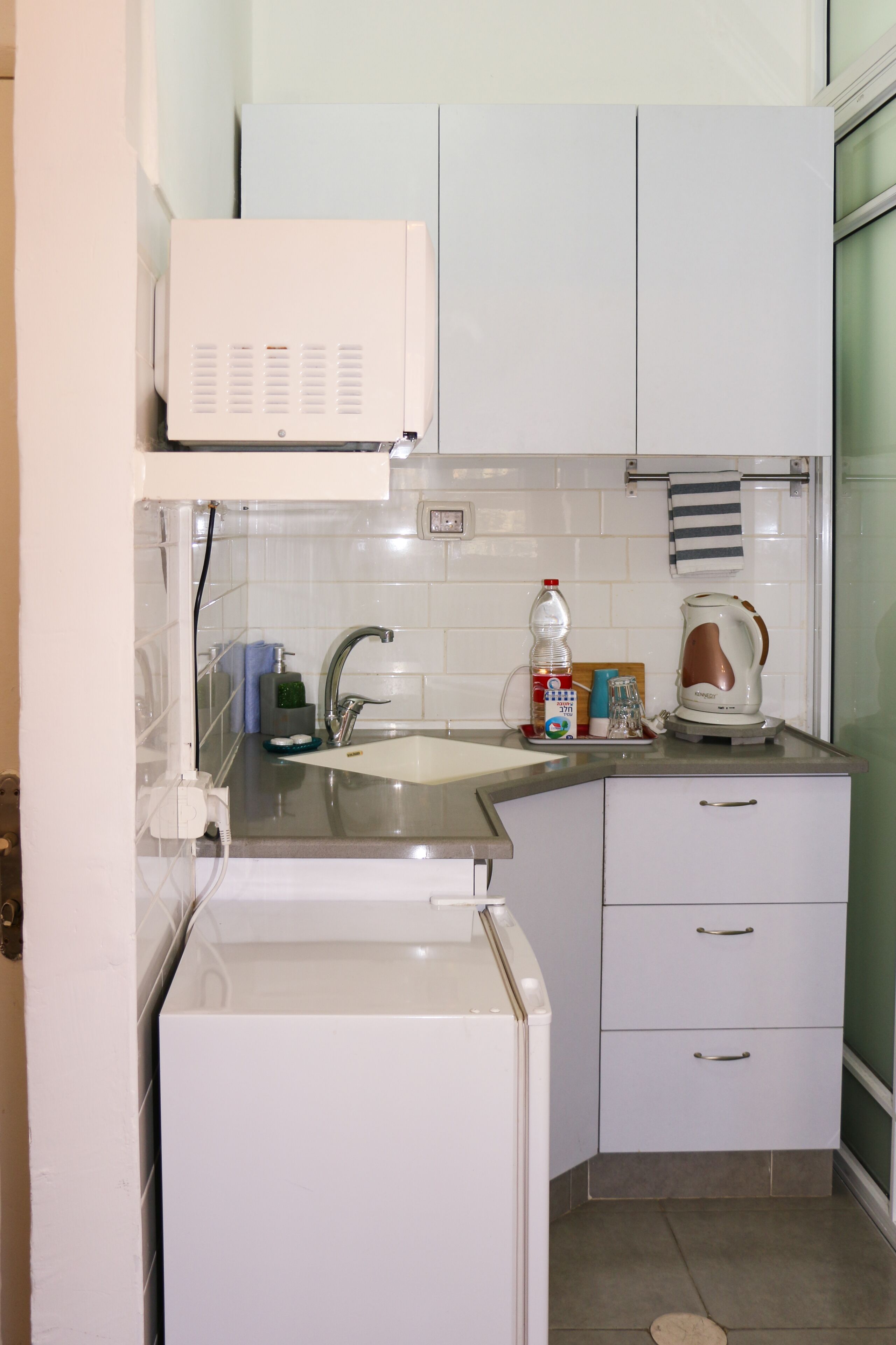 Una cocina compacta con microondas integrado, un lavamanos y un hervidor.