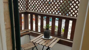 A balcony with a wooden table and chairs, a potted plant, and a lattice fence.