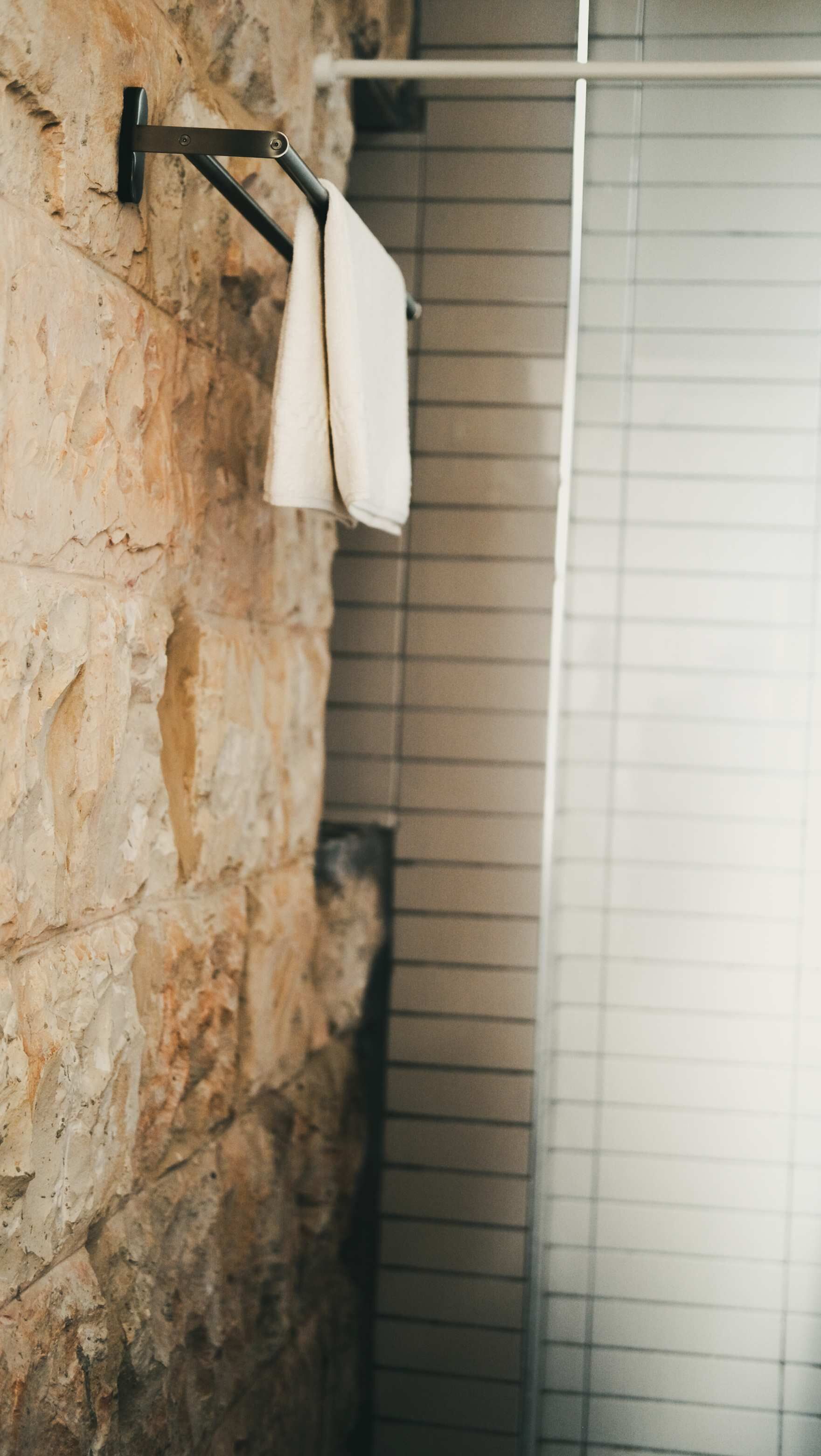 A bathroom with a stone wall, a towel rack, and a shower area.