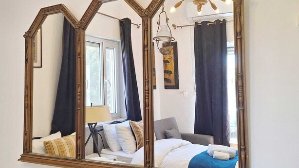 A bedroom with a large mirror, a bed with white bedding, a bedside table, and a lamp. - Tzefania Hotel (Jerusalem)