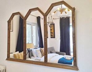 A bedroom with a large mirror, a bed with white bedding, a bedside table, and a lamp. - Tzefania Hotel (Jerusalem)