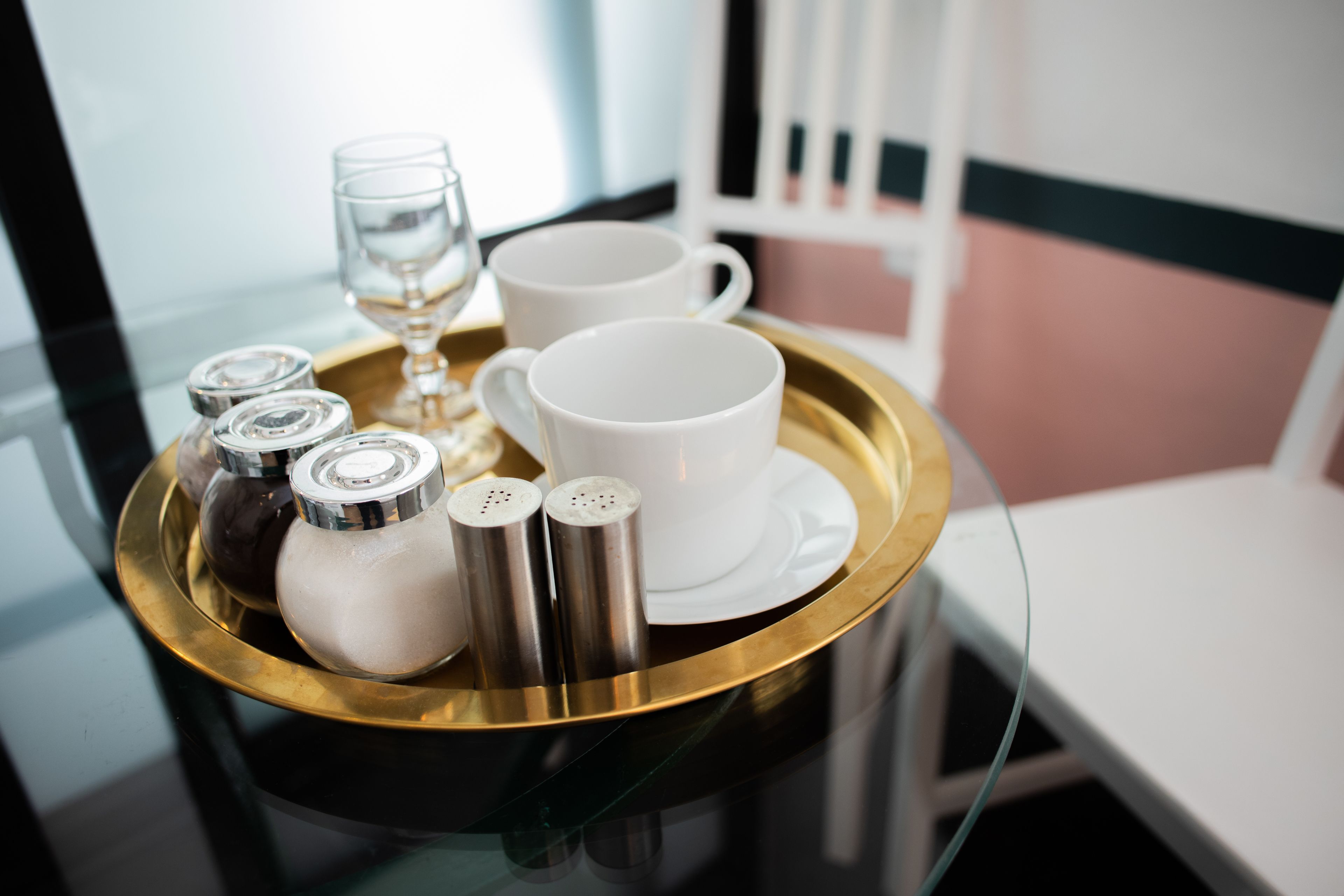 A tray with salt and pepper shakers, a glass, and two white cups on a reflective surface.