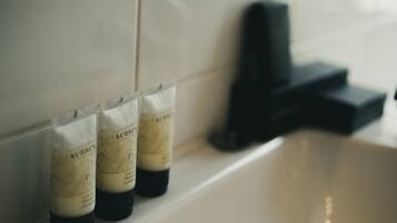 Un baño con un lavamanos blanco, un grifo negro y tres botellas de champú con la etiqueta 'senses' en la pared.