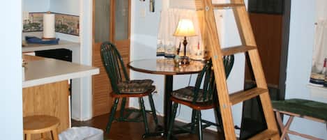 A cozy room with a wooden ladder, a dining table with chairs, a small kitchen area, and a patterned floor.