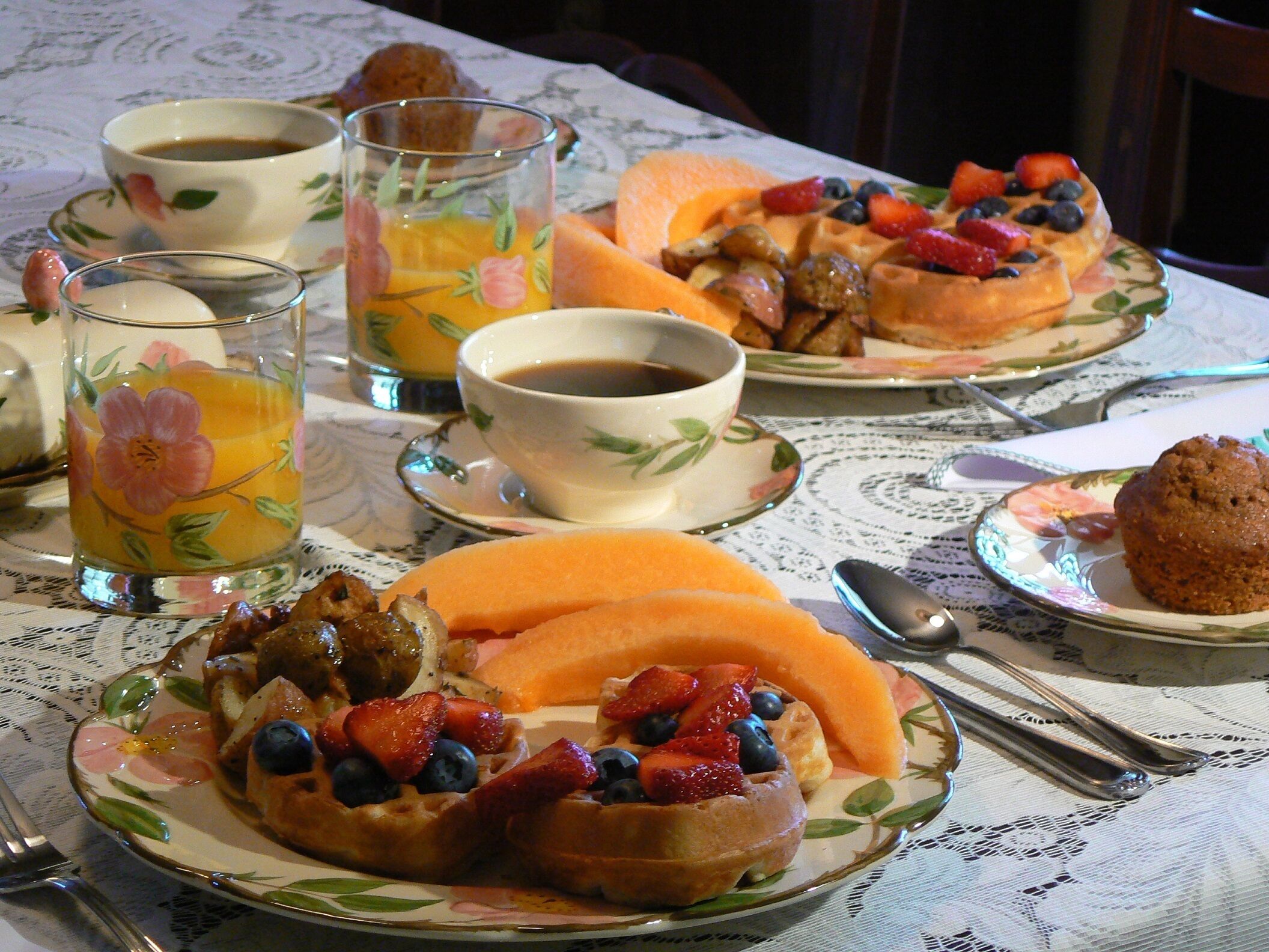 Ein Frühstückstisch mit Waffeln, Früchten und Kaffee, gedeckt mit einer Tischdecke aus Spitze.