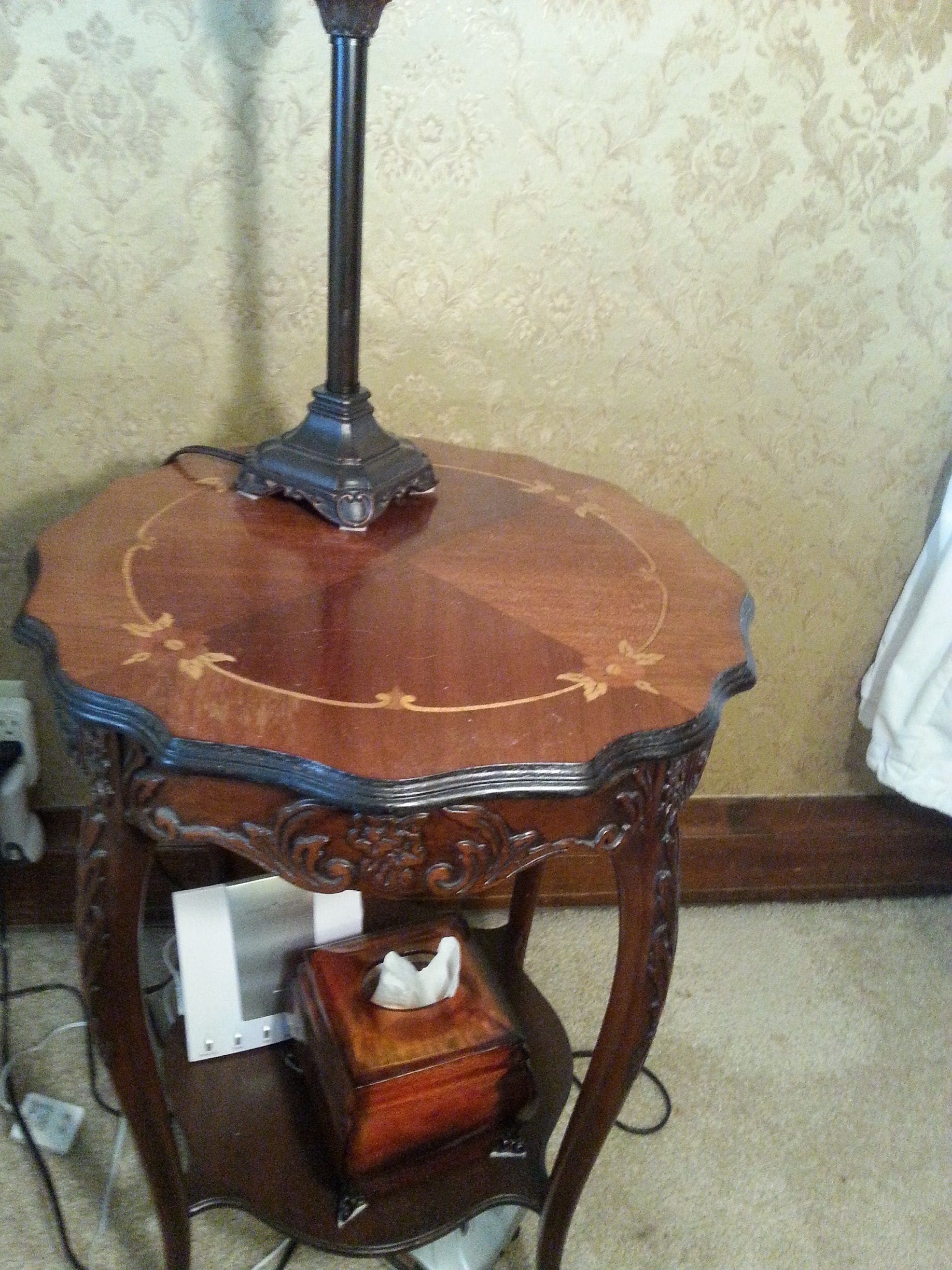 A wooden side table with a lamp, a tissue box, and a power cord.