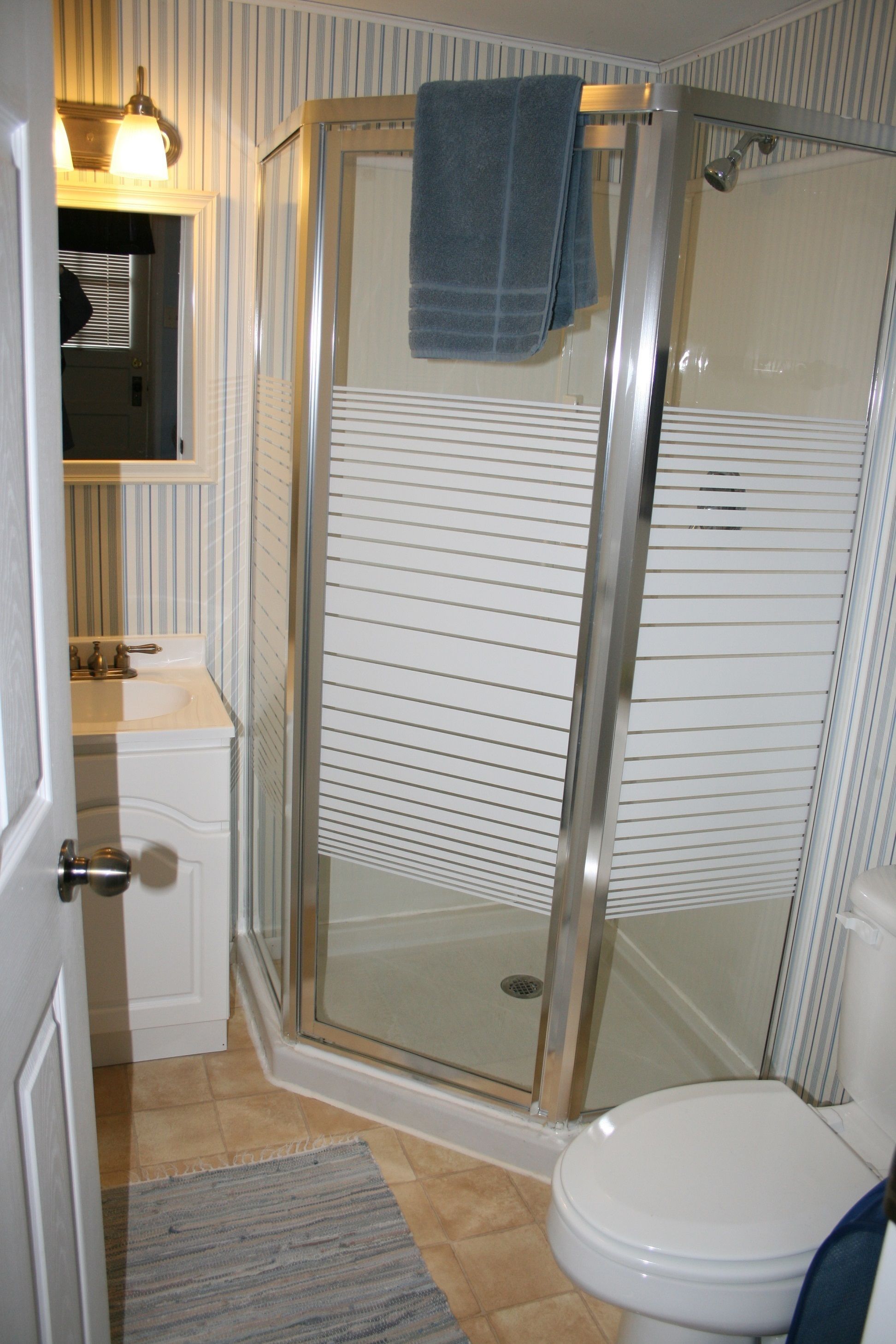 A bathroom with a glass shower enclosure, a white toilet, a sink with a mirror, and striped wall tiles.