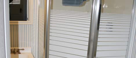 A bathroom with a glass shower enclosure, a white toilet, a sink with a mirror, and striped wall tiles.
