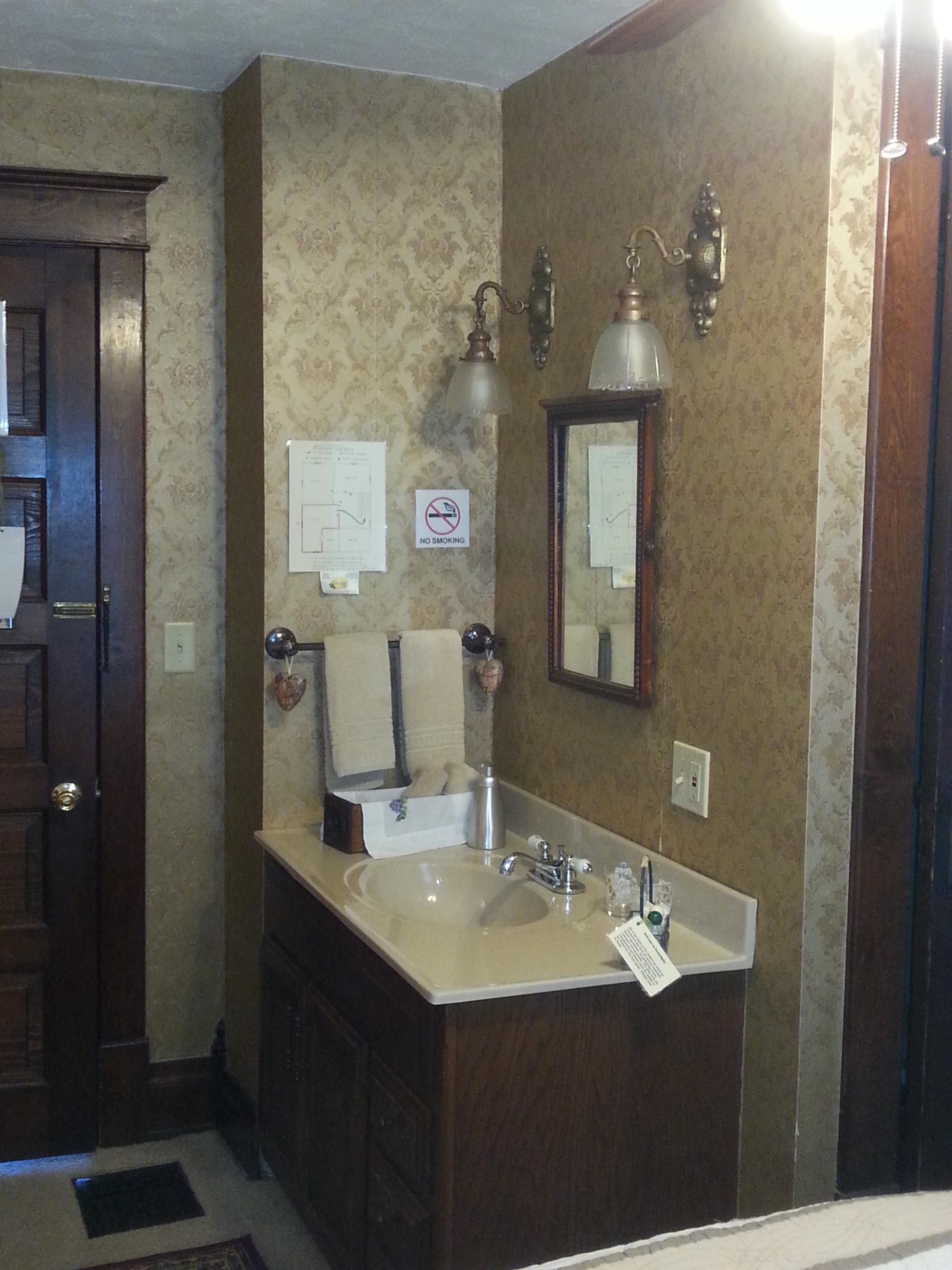 Un baño con tocador de madera, un lavabo y un espejo. Hay un letrero de 'No Fumar' en la pared.