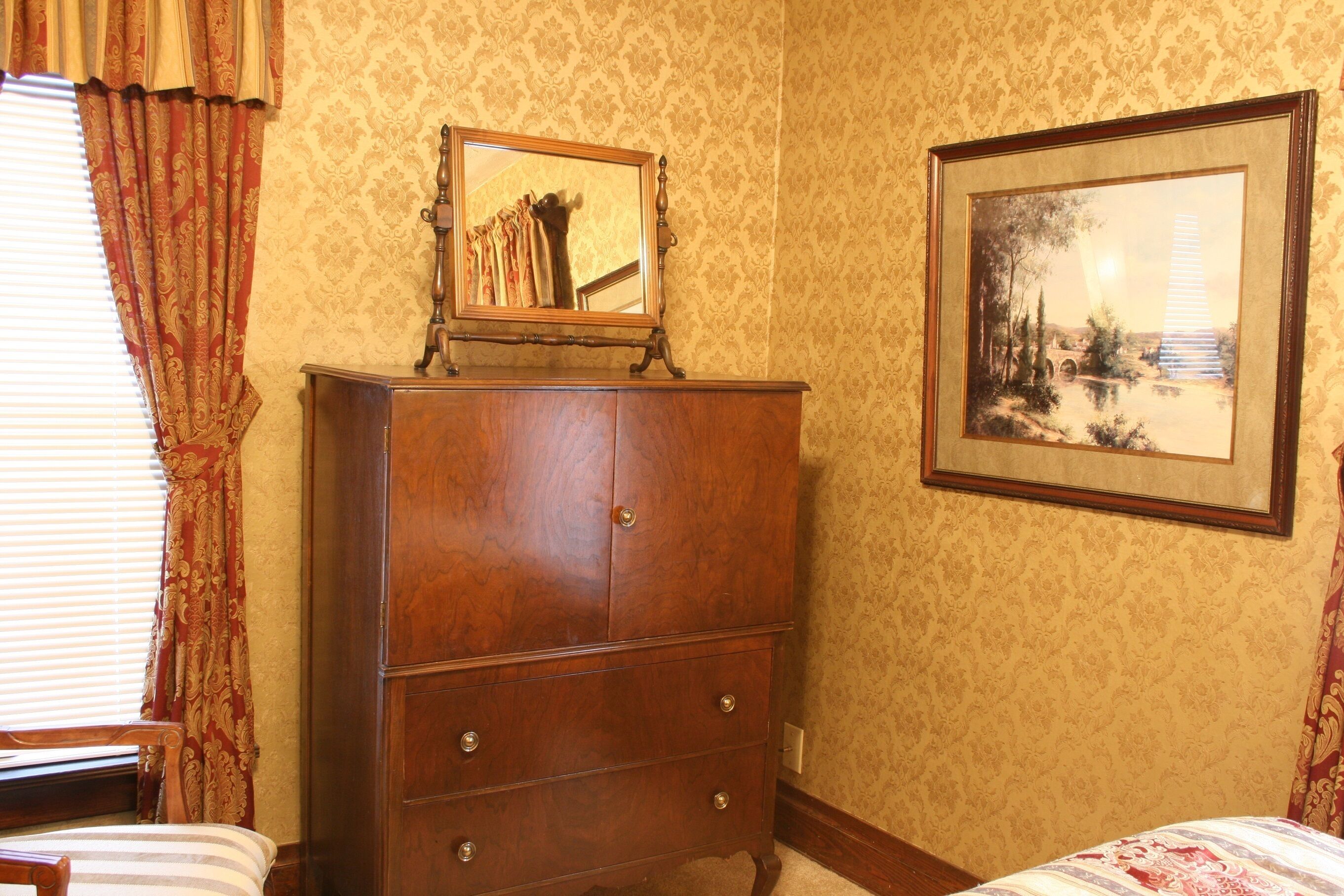 A bedroom with a wooden dresser, a bed with striped bedding, and two framed pictures on the wall.
