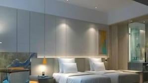 Een moderne slaapkamer met een groot bed, nachtkastjes, een stoel en een glazen scheidingswand.