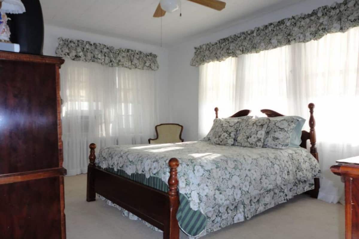 Une chambre à coucher avec un lit en bois, une table de chevet, une chaise et un ventilateur de plafond.