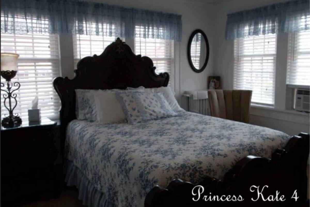 Une chambre à coucher avec un grand lit, une commode, un miroir et une fenêtre avec des stores.