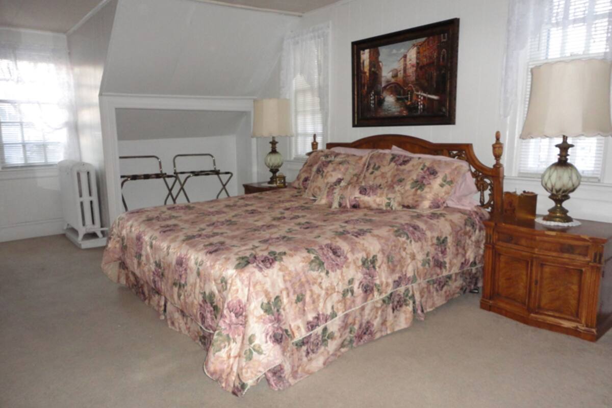 Une chambre à coucher avec un lit, une table de chevet, une lampe, un radiateur et un tableau au mur.