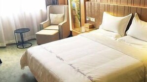 A hotel room with a large bed, a chair, a small table, and a view of the outdoors. - West Lake Hotel (Shenzhen)