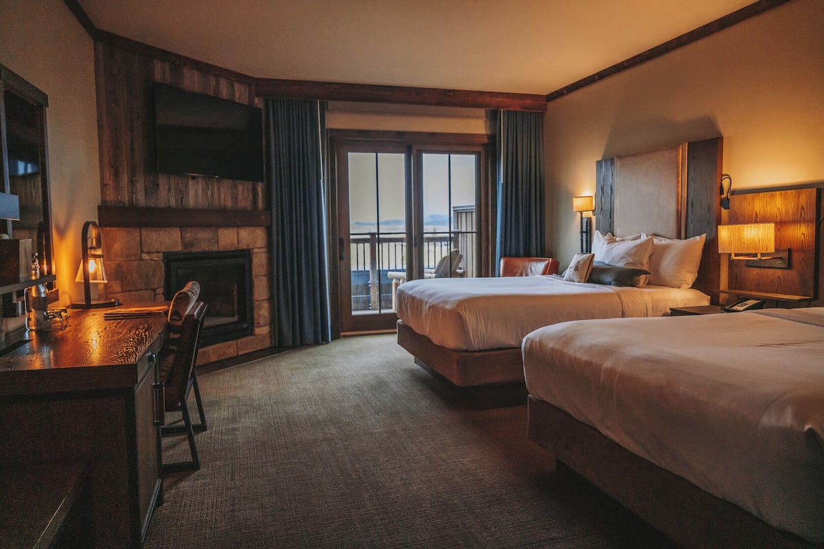 A hotel room with two beds, a desk, a fireplace, and a balcony with a view.