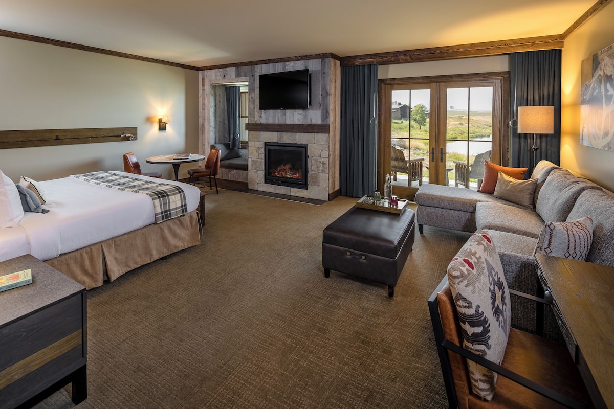 A hotel room with a bed, a sofa, a fireplace, a TV, and a view of the outdoors.