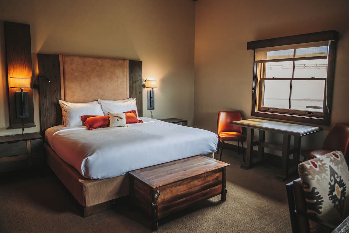 A hotel room with a large bed, a wooden bench, a desk, and a chair.