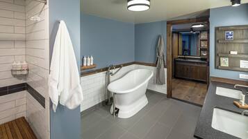 A modern bathroom with a freestanding bathtub, a wooden bench, and a vanity with two sinks.