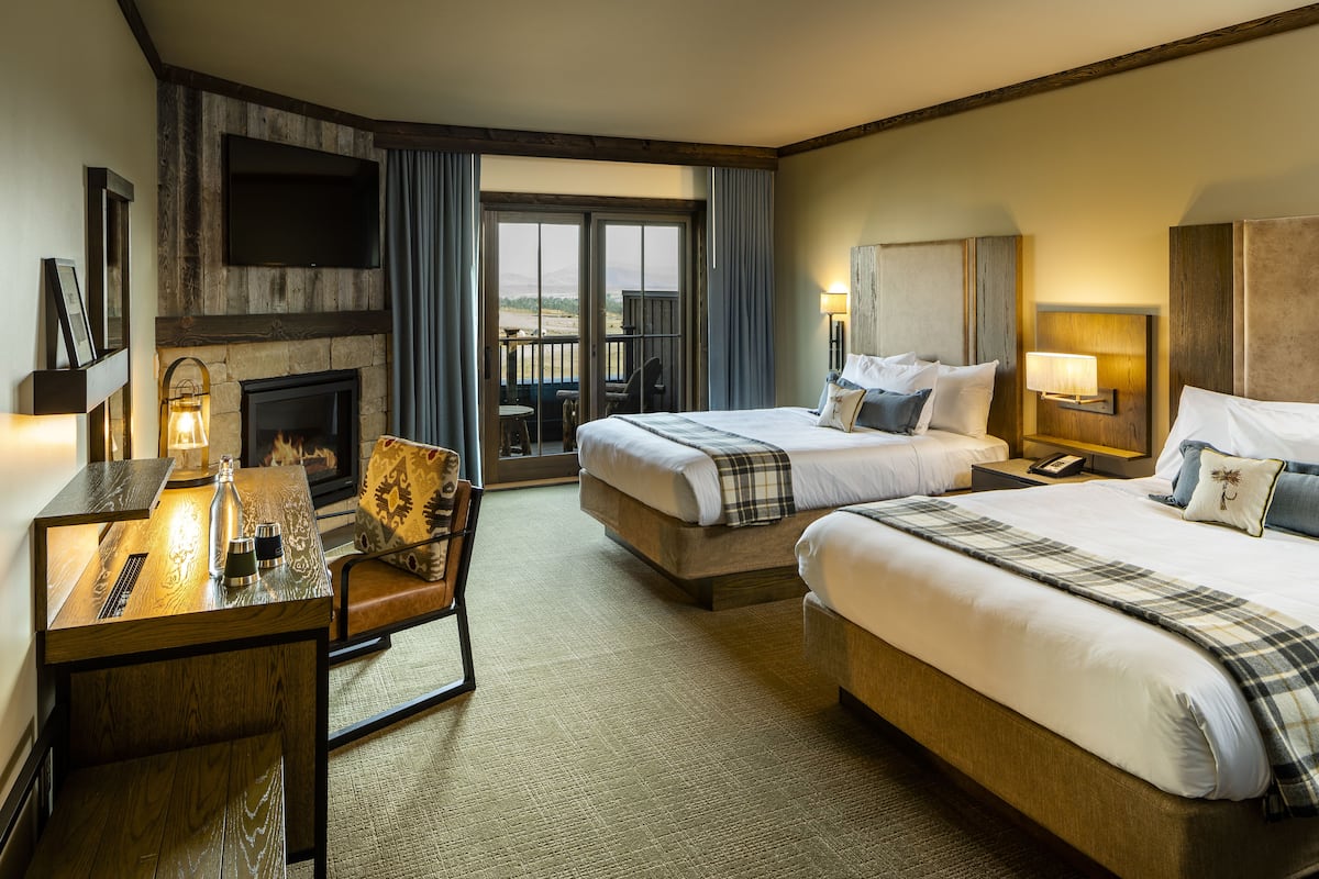 A hotel room with two beds, a fireplace, a television, and a balcony with a table and chairs.