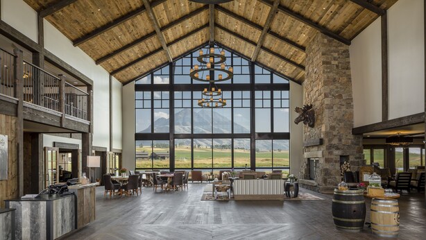 Un vestíbulo espacioso con techo alto, ventanas amplias que ofrecen vistas a la montaña, una chimenea de piedra y un mostrador de recepción.