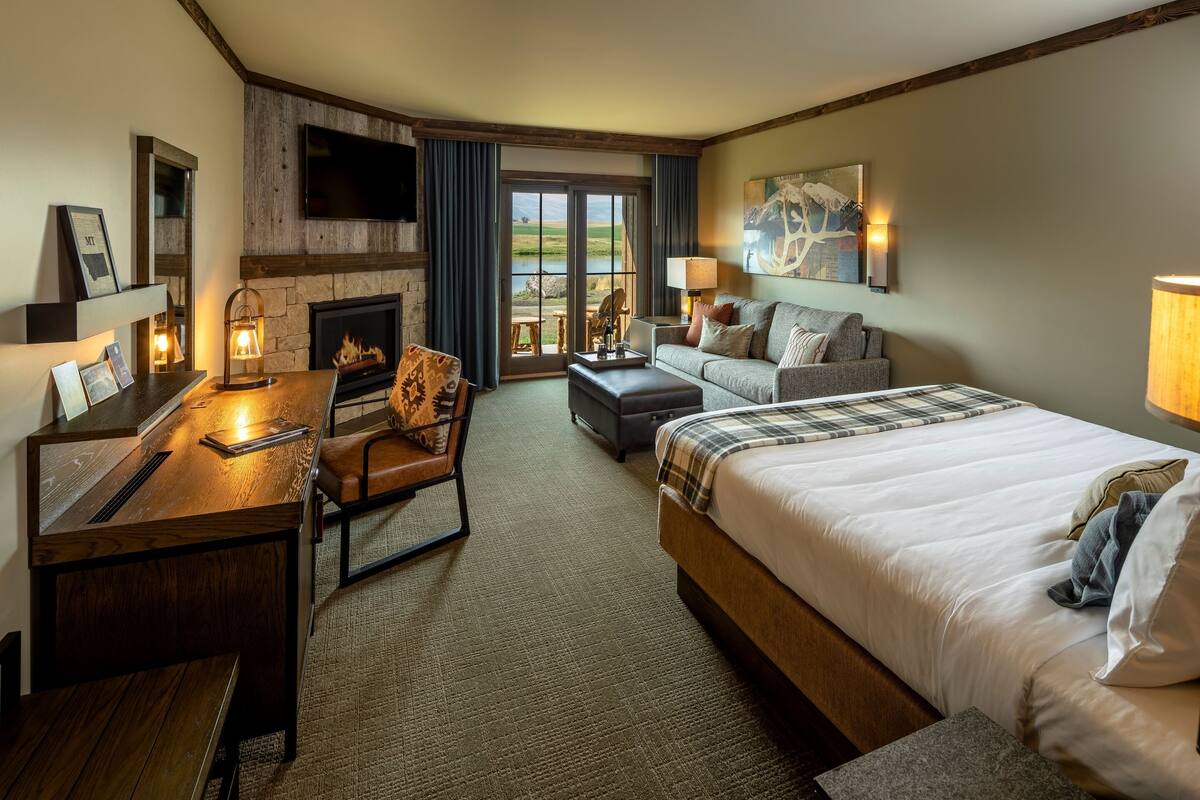 A hotel room with a fireplace, a sofa, a bed, a desk, and a view of the outdoors.