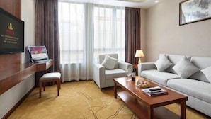 A hotel room with a sofa, a coffee table, a TV, and a desk with a computer.