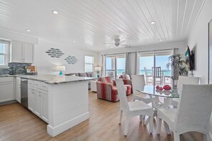 A modern kitchen with white cabinetry, a marble countertop, and a dining area with a glass table and white wicker chairs. - Eastern Shores - 206 1 Bedroom Condo by RedAwning (Santa Rosa Beach)