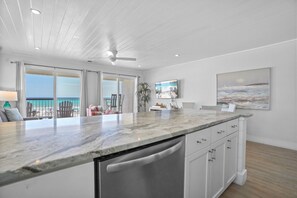 A modern kitchen with a large island, white cabinetry, and a view of the beach. - Eastern Shores - 206 1 Bedroom Condo by RedAwning (Santa Rosa Beach)