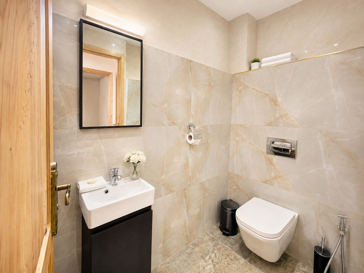 Un baño con pared de mármol, un lavabo, un inodoro, un cubo de basura y una ducha.