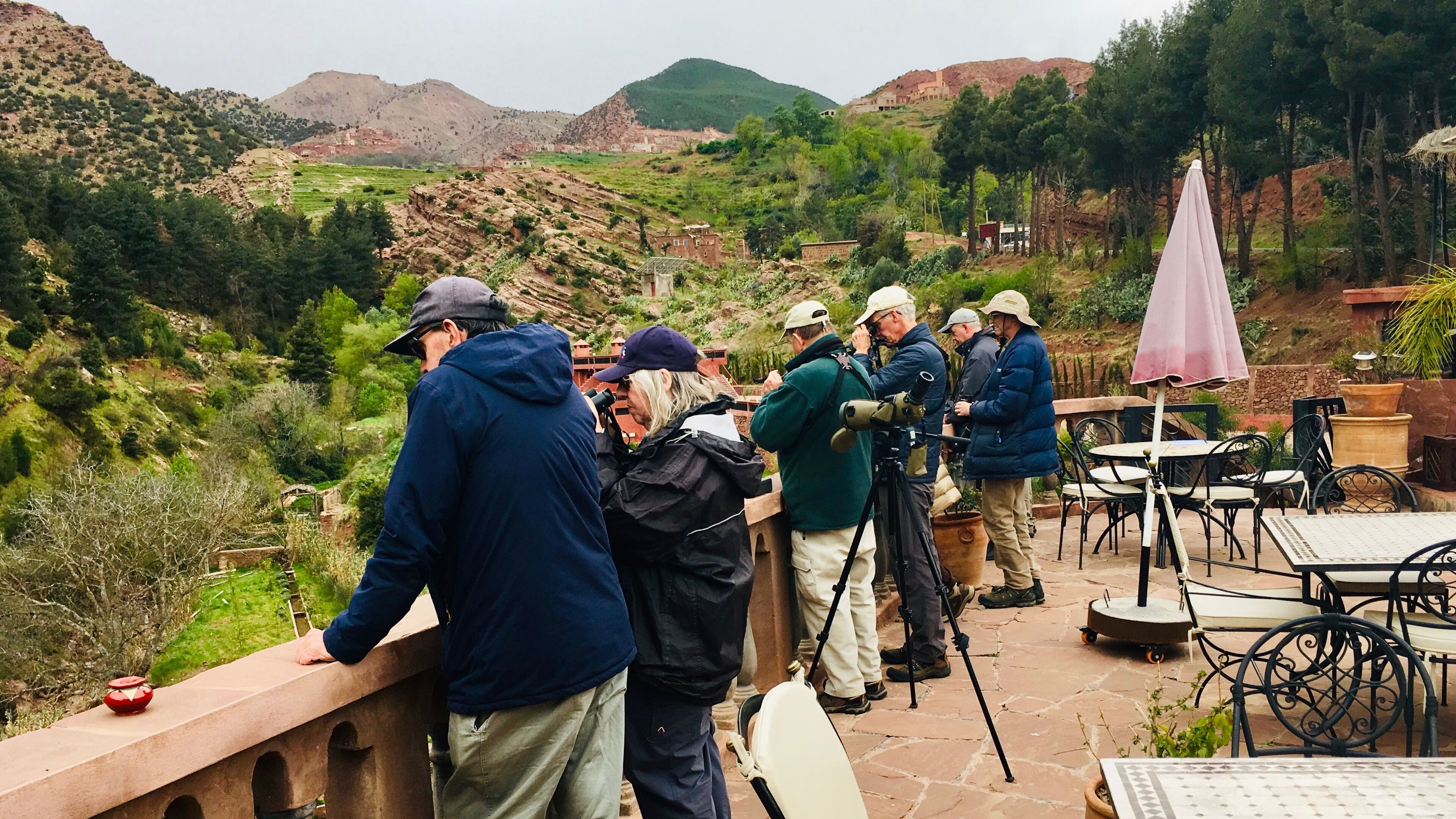 Un grupo de personas de pie en una terraza con vistas a un paisaje montañoso.