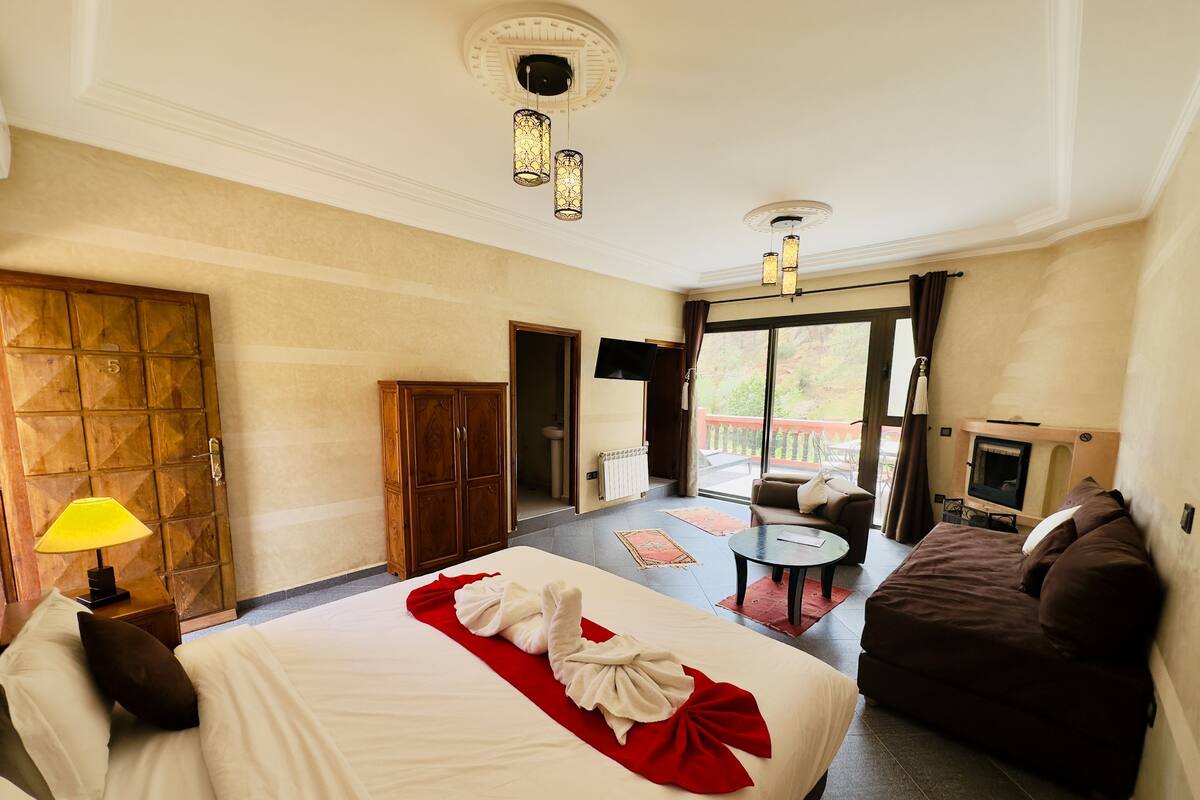 A hotel room with a large bed, a sofa, a small table, a TV, and a balcony with a view.